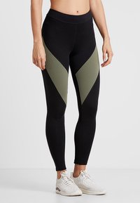 Leggings noirs avec des panneaux en chevron vert olive. Fabriqués à partir d'un tissu extensible, dotés d'une taille haute et d'un design élégant.