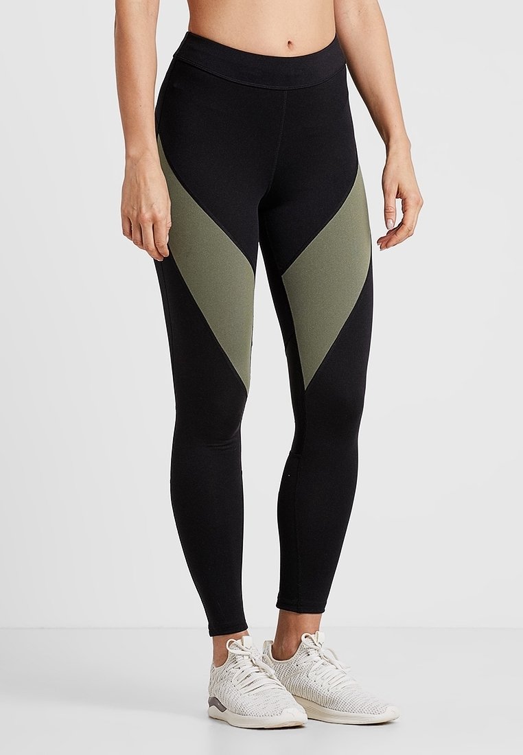 Leggings noirs avec des panneaux en chevron vert olive. Fabriqués à partir d'un tissu extensible, dotés d'une taille haute et d'un design élégant.