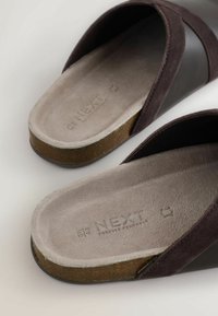 Sandalias tipo slide de ante marrón con una suave correa de cuero negro y una suela de corcho. El interior presenta una textura suave gris con marca.