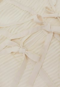 Helebeež kangas horisontaalsete triipudega. Omab mitmeid kangast lipsu kujulisi sidumisnööre, mis lisavad tekstuuri ja detaile üldilmele.