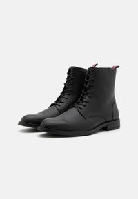 Botas de cuero negras hasta el tobillo con una textura suave, cordones en la parte delantera, puntera redondeada y una tira de sujeción a rayas en el talón que contrasta.