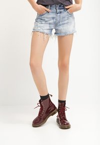 Denimshorts med fransad nederkant i ljusblått, matchat med glansiga maroon snörstövlar som har gyllene ögla och en svart strumpa.