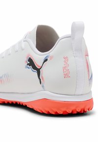 Weißer Sportschuh mit strukturiertem orangefarbenem Sohlen, schwarzem Puma-Logo und bunten Akzenten in Blau und Rot. An der Rückseite befindet sich eine Zuglasche und Branding.