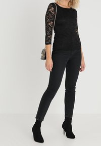 Black lace top with three-quarter sleeves, fitted design, paired with black skinny jeans and black heeled ankle boots. Small metallic bag.