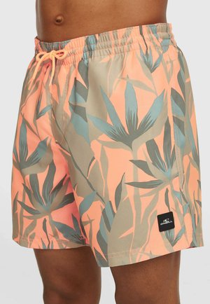 Man draagt koraalroze en groene zwemshorts met tropisch bladprint, elastische tailleband en trekkoord, met een zwart O'Neill-logo op de zoom.