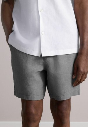 Shorts en lin gris avec une coupe décontractée et un ourlet droit, assortis à une chemise blanche à manches courtes avec boutons. La texture est douce et légère.