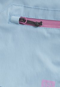 Ljust blått tyg med en rosa dragkedja och en svart dragsnodd. Innehåller sydda detaljer och en liten rosa logotyp i nedersta högra hörnet.