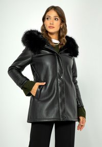 Zwarte neplederen jas met een met bont gevoerde capuchon, voorzien van een knoopsluiting, zijzakken en een gestructureerde pasvorm. Geaccentueerd met groene trui-mouwen.