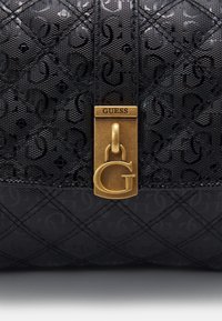 Černá kožená kabelka s prošívaným vzorem, embosovanými logy a zlatým visacím zámkem s přívěskem ve tvaru „G“. Odolná textury a elegantní design.