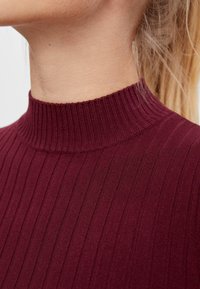 Burgundy ribbad polokrage tröja med hög krage, som har en strukturerad yta och en åtsittande passform, som framhäver vertikalt placerade ränder.