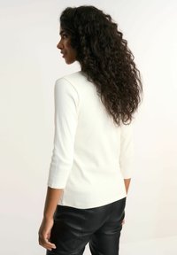 Lekki, biały, prążkowany top z rękawami o długości trzech czwartek, zestawiony z czarnymi skórzanymi spodniami. Top ma okrągły dekolt i dopasowany krój.