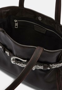 Brązowa skórzana torebka o gładkiej fakturze, wyposażona w srebrną klamrę i zdobienia. Wewnątrz znajduje się kieszeń na zamek oraz czarna podszewka.