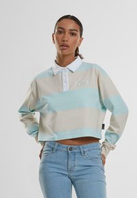 Polo à manches longues coupé en beige clair avec des rayures aqua ; il possède un col blanc et un logo brodé. Matière en coton et coupe décontractée.