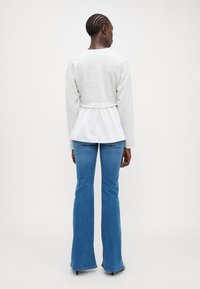 Sudadera gris recortada con un panel blanco en la parte posterior, combinada con jeans azules acampanados. Tejido suave, cintura elástica y dise�ño simple.