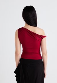 Top bordeaux a una spalla in tessuto elasticizzato, con dettagli drappeggiati e silhouette aderente, abbinato a una gonna nera a strati.