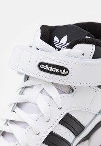 Witte leren sneaker met zwarte accenten, voorzien van drie strepen, gevoerde kraag, vetersluiting en verstelbare klittenbandsluiting.