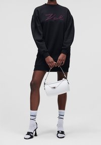 Robe sweat noire avec texte brodé rose, associée à un sac à main blanc, des escarpins noirs et des chaussettes grises avec texte bleu.