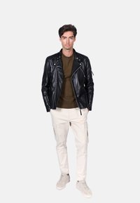 Czarna skórzana kurtka motocyklowa z zamykanymi kieszeniami, oliwkowy sweter, jasnobeżowe spodnie cargo i jasnoszare sneakersy.