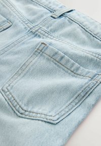 Materialul din denim albastru deschis are un buzunar din spate cu un model subtil de cusături și o suprafață texturată, evidențiind designul său casual.