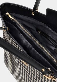 Sac à main en pied-de-poule noir et blanc avec des poignées noires, compartiment à fermeture éclair ouvert et doublure intérieure de marque.