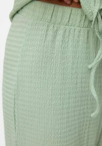 Ljust gröna texturerade joggers med ett vågigt mönster, elastisk midja och snörningsdetalj. Tyget verkar mjukt och lätt.