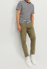 Koszula w paski z krótkim rękawem w kolorach granatowym i kremowym z okrągłym dekoltem, zestawiona z oliwkowozielonymi wąskimi spodniami i białymi trampkami.