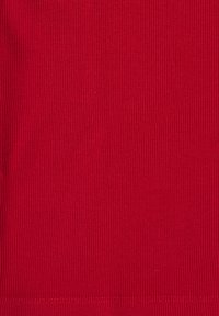 Gros plan sur la texture d’un tissu rouge côtelé avec des lignes verticales et une couture horizontale près du bord inférieur.