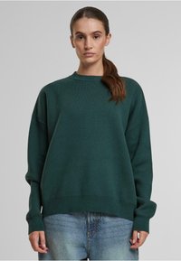 Dunkelgrüner, übergroßer Pullover mit Rundhalsausschnitt, gerippten Bündchen und einer weichen Textur, kombiniert mit hellblauen Jeans.