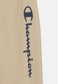 Μπεζ βαμβακερό jogger με υφή, με σκούρο ναυτικό μπλε λογότυπο κατά μήκος της πλευράς. Απαλή, άνετη εφαρμογή για άνεση.