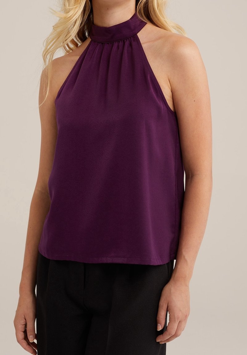 Top violet à encolure halter en tissu lisse, avec des plis au niveau du col et une coupe décontractée. Assorti à un pantalon noir.