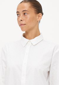 Hvit skjorte med krage, med subtile teksturerte prikker over hele stoffet. Lange ermer, klassisk passform og knappet front.