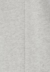 Primer plano de una tela gris claro con una costura vertical central, mostrando una textura de punto y un sutil patrón jaspeado.