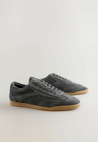 Tenisi gri din suede cu profil jos, având un superior texturat, vârf rotund și talpă din gumă de culoare caramel. Design clasic cu șireturi.