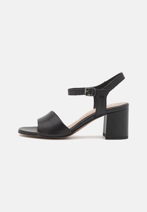 Sandale noire en cuir à bout ouvert avec bride à la cheville, boucle argentée et petit talon bloc, présentée de profil sur fond blanc.