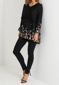 Svart blommig tunika med långa ärmar, volangkant och knappear. Matchas med svarta skinny jeans och öppna klackar.