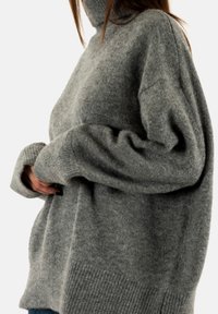 Pull en col roulé gris en tissu doux et texturé ; il possède des manches larges et un ourlet côtelé pour un ajustement ample et confortable.