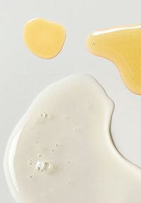 Drie vlekken vloeistof op een lichte achtergrond: een heldere, stroperige vloeistof met belletjes en twee gladde, amberkleurige druppels.