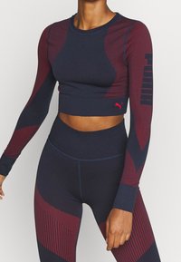 Marineblaues und kastanienbraunes langärmliges Cropped-Top mit strukturierten Einsätzen, kombiniert mit hochgeschnittenen Leggings, die geometrische Muster und kontrastierende Nähte aufweisen.