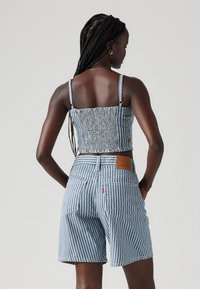 Top cropped em azul e branco com riscas, com textura franzida e alças finas, combinado com calções de ganga de cintura alta com um patch de pele.