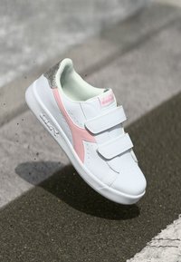 Baskets blanches avec un accent rose et un onglet de talon texturé en argent. Dotées de deux fermetures Velcro et de perforations sur le bout pour la respirabilité.