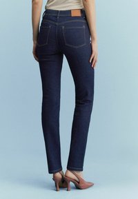 Slim-fit mörkblå denimjeans med en läderlapp på baksidan, som har två bakfickor och fållade ben, kombinerat med rosa klackskor.