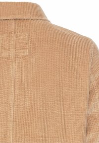 Gros plan sur un tissu en velours côtelé beige montrant des rainures verticales et une partie de col d'un vêtement.