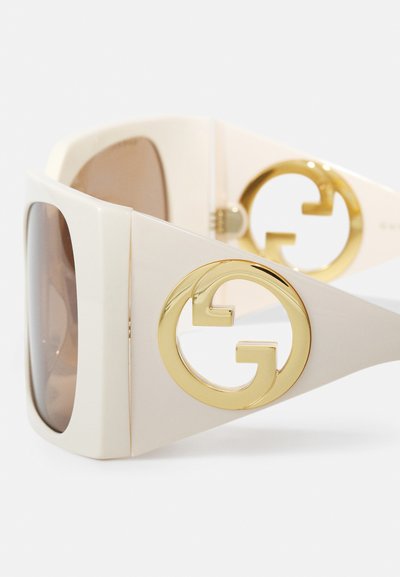 Gafas de sol oversize de marfil con lentes marrones, que cuentan con un prominente logo GG dorado en las patillas y un acabado suave y brillante.