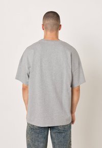 Šedé tričko s krátkým rukávem z bavlny, s pohodlným střihem, minimalistickým designem a kulatým výstřihem. Nositelná s modrými džínovými kalhotami.