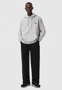 Hanorac gri cu glugă, buzunar frontal și șnururi, asortat cu pantaloni negri și adidași negri, având un logo simplu pe piept.