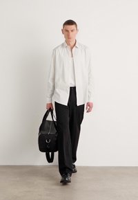 Camisa blanca de botones, pantalones negros y zapatos negros. Lleva un bolso negro con asas superiores. Diseño sencillo, tela ligera y una paleta de colores neutros.
