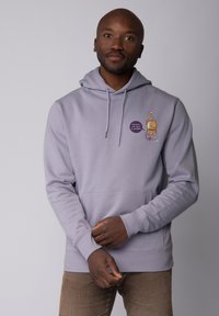 Lichtgrijze hoodie met een voorzak, trekkoorden en geborduurde graphics, waaronder een personage en tekstdetail.
