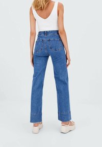 High-waisted blauwe denim jeans met een recht model, voorzien van achterzakken en een opgerolde zoom. Draagt een fitted witte top.