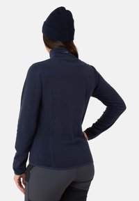 Jaket fleece navy dengan kerah tinggi dan lengan panjang, menampilkan tekstur halus dan hem melengkung. Disertai dengan topi beanie yang serasi.