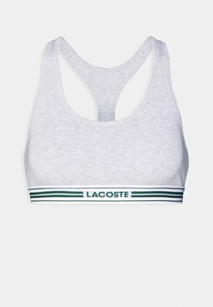 Grauer Sport-BH mit Rundhalsausschnitt und Racerback-Design. Mit einem Band mit "LACOSTE"-Logo und grünen Streifen am unteren Rand. Weiche Textur.
